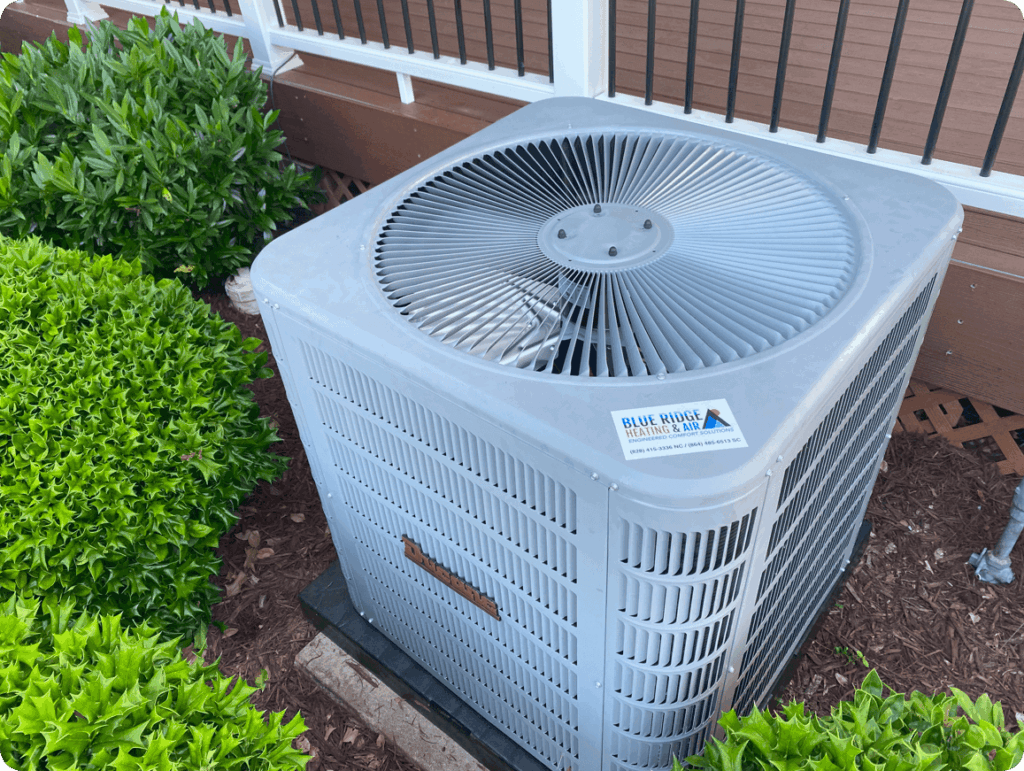 Blue Ridge Heating & Air heat pump unit installed outdoors next to a wooden deck with green shrubs