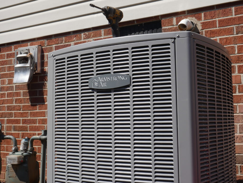 Armstrong Air outdoor AC condenser unit installed against a brick wall